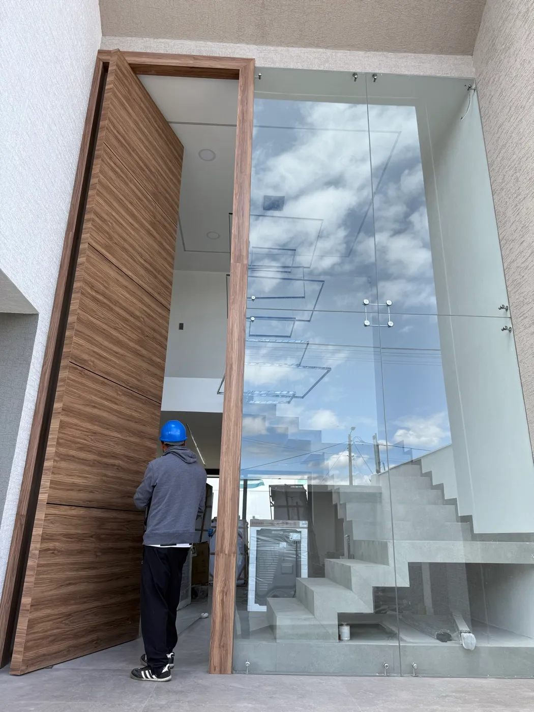 Puerta pivotante de madera y vidrio de doble altura en el acceso